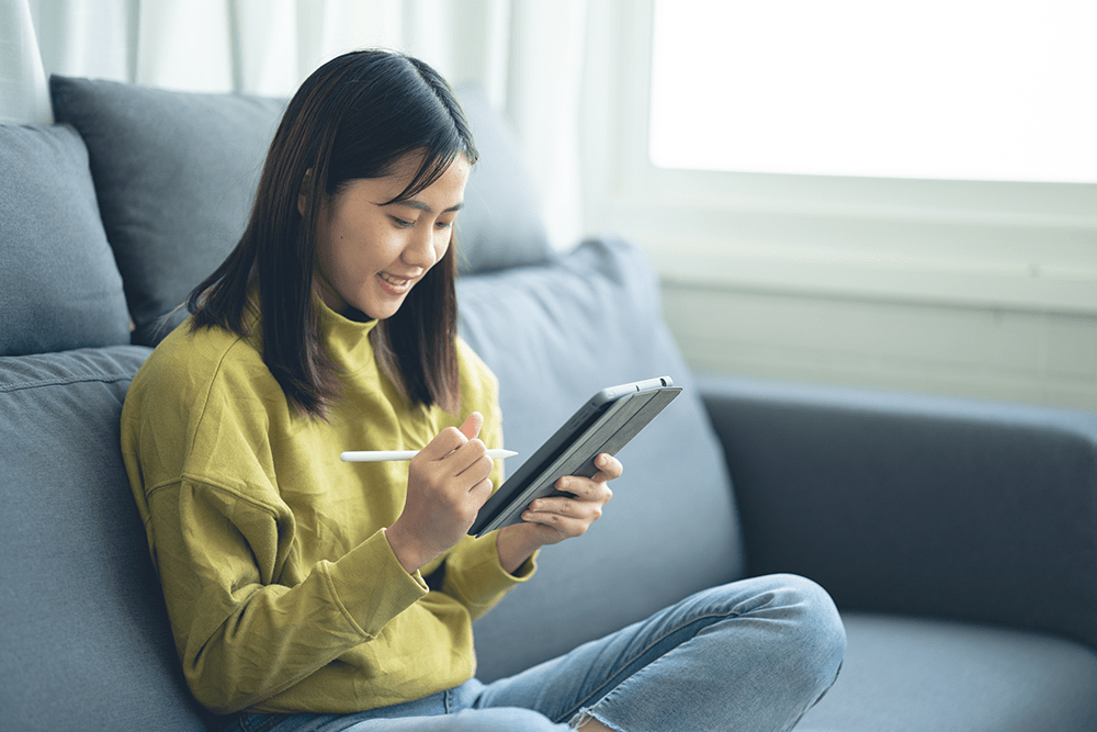 An Asian woman sitting on a tablet on a sofa 脱『勉強机』で個別学習を強化